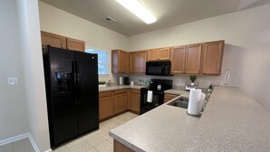 A kitchen with wooden cabinets, a black refrigerator, a microwave, and a granite countertop. - Inviting and Relaxing Beach and Golf Condo (North Myrtle Beach)