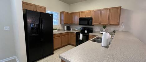 A kitchen with wooden cabinets, a black refrigerator, a microwave, and a granite countertop.