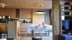Une cuisine chaleureuse avec des meubles en bois, une table à manger pour quatre personnes et une bibliothèque remplie de livres.