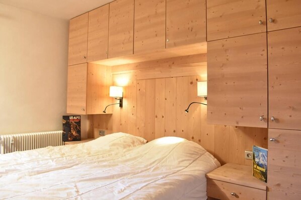 A bedroom with a wooden headboard, two bedside lamps, a bed with white bedding, a radiator, and a book on a nightstand.