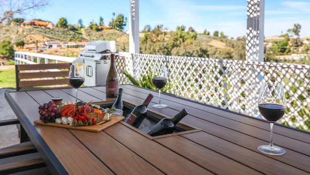 A wooden table with a charcuterie board, wine bottles, and glasses on an outdoor patio with a white lattice fence and a scenic view. - 2 Patios, BBQ, Center Wine Country (Temecula)