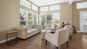 A spacious living room with a beige sofa, a round coffee table, and a chair. Large windows with blinds allow natural light to enter. - 2 Patios, BBQ, Center Wine Country (Temecula)