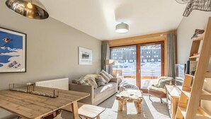 Un salon chaleureux avec une table à manger en bois, un canapé et une table basse. Une fenêtre offre une vue sur un paysage enneigé.