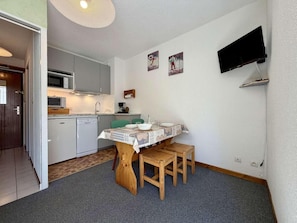 Una cocina compacta con una mesa de comedor, sillas y un televisor instalado en la pared.