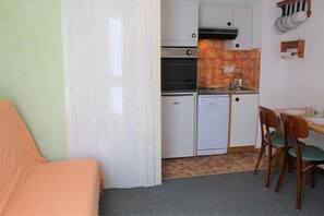 A compact kitchen with a dishwasher, stove, and a small refrigerator. There is a dining table with chairs and a single bed in the room. - 100m from ski slopes, 4th floor, tv, ski locker, 18m², Vars (Vars)