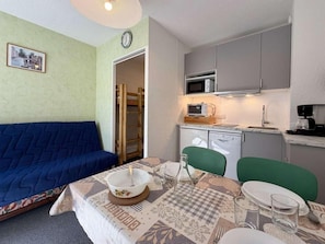 Un espacio habitable compacto con sofá, mesa de comedor, sillas, microondas y una pequeña kitchenette.