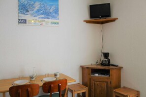 A small dining area with a wooden table, four chairs, a coffee maker, and a television on a shelf above the table. - 100m from ski slopes, 4th floor, tv, ski locker, 18m², Vars (Vars)