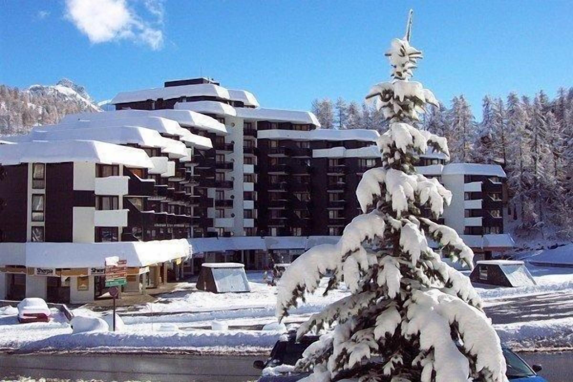 A multi-story hotel with a snow-covered exterior, a parking area, and a snow-laden tree in the foreground.