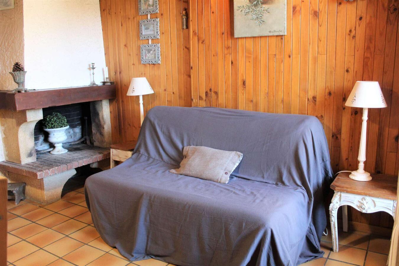 Ein gemütliches Zimmer mit einem Bett, das mit einer grauen Decke bezogen ist, zwei Nachttischlampen, einem Kamin und Holzwänden.
