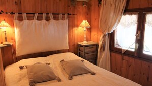 Une pièce en bois avec un lit, deux oreillers, une table de chevet avec une lampe et une fenêtre avec des rideaux.