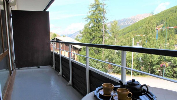 A balcony with a view of a mountainous landscape, a table with a tray holding two cups and a teapot.