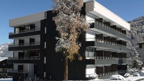 A modern multi-story building with balconies, surrounded by snow-covered ground and a clear sky.
