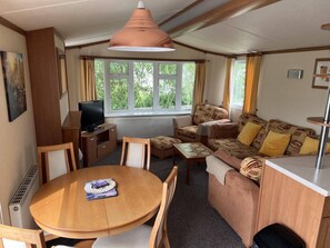 A cozy living room with a wooden table, a sofa, and a television. - Cozy  2 bedroom Coastal Chalet in Hunstanton (Hunstanton)