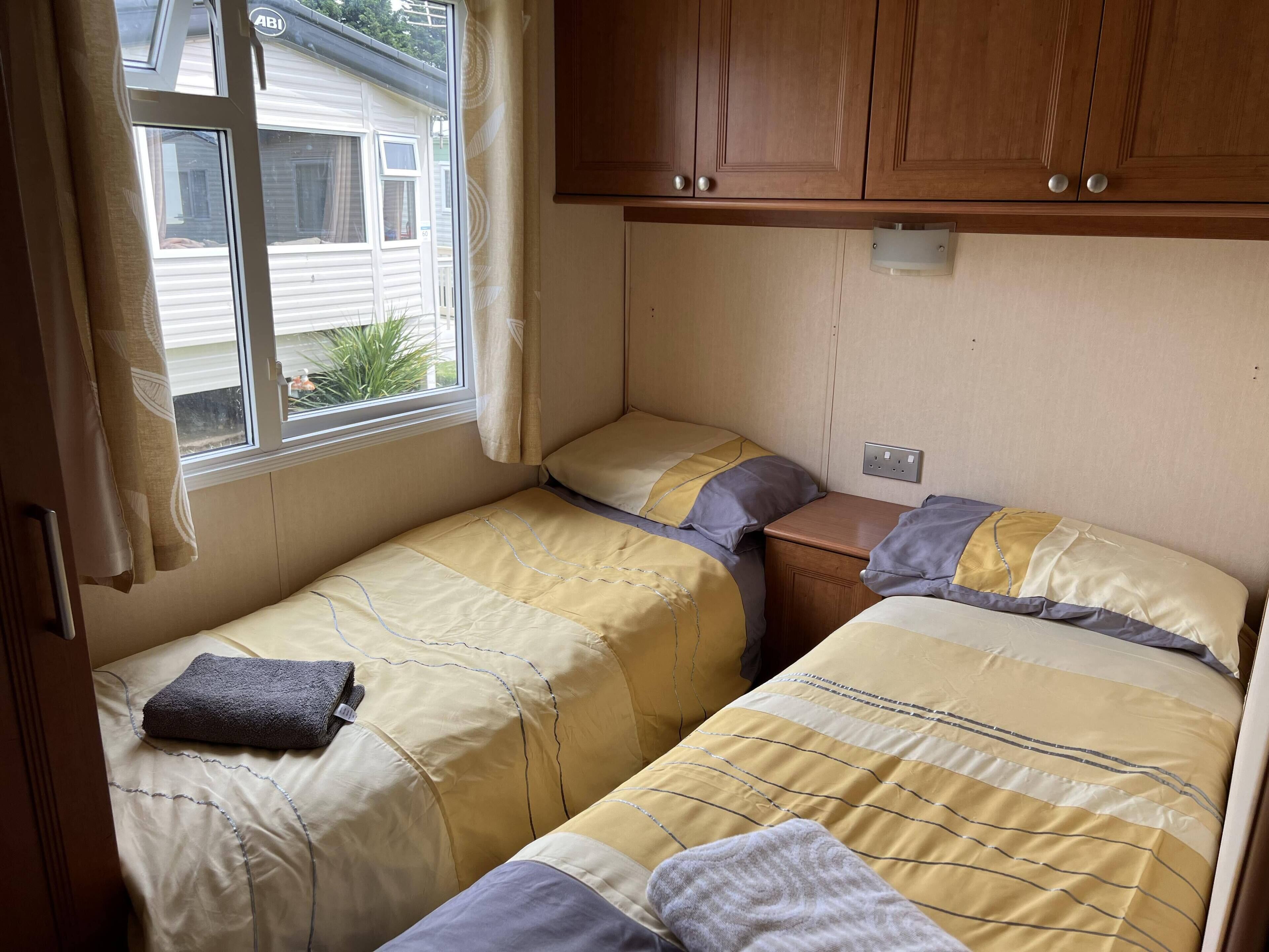 Un dormitorio pequeño con dos camas, armarios de madera, una ventana con cortinas y un enchufe en la pared.