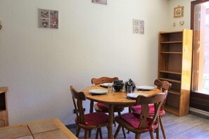 Un'area pranzo con un tavolo in legno apparecchiato per quattro, circondato da sedie in legno con cuscini rossi. Sopra il tavolo ci sono decorazioni a parete e, a destra, una libreria in legno.