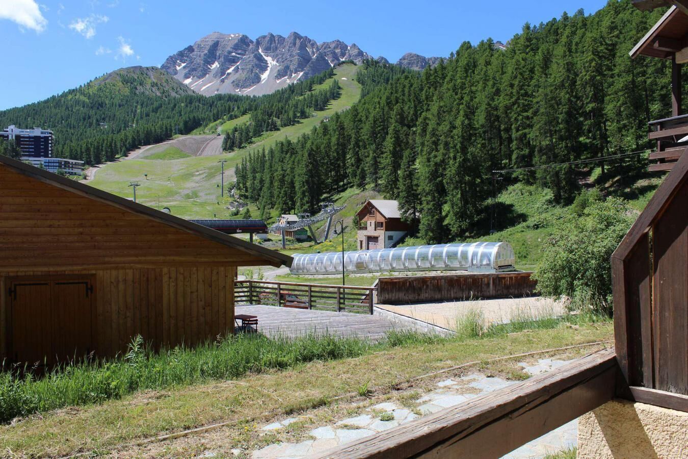 A wooden cabin with a view of a mountain range and a greenhouse structure.