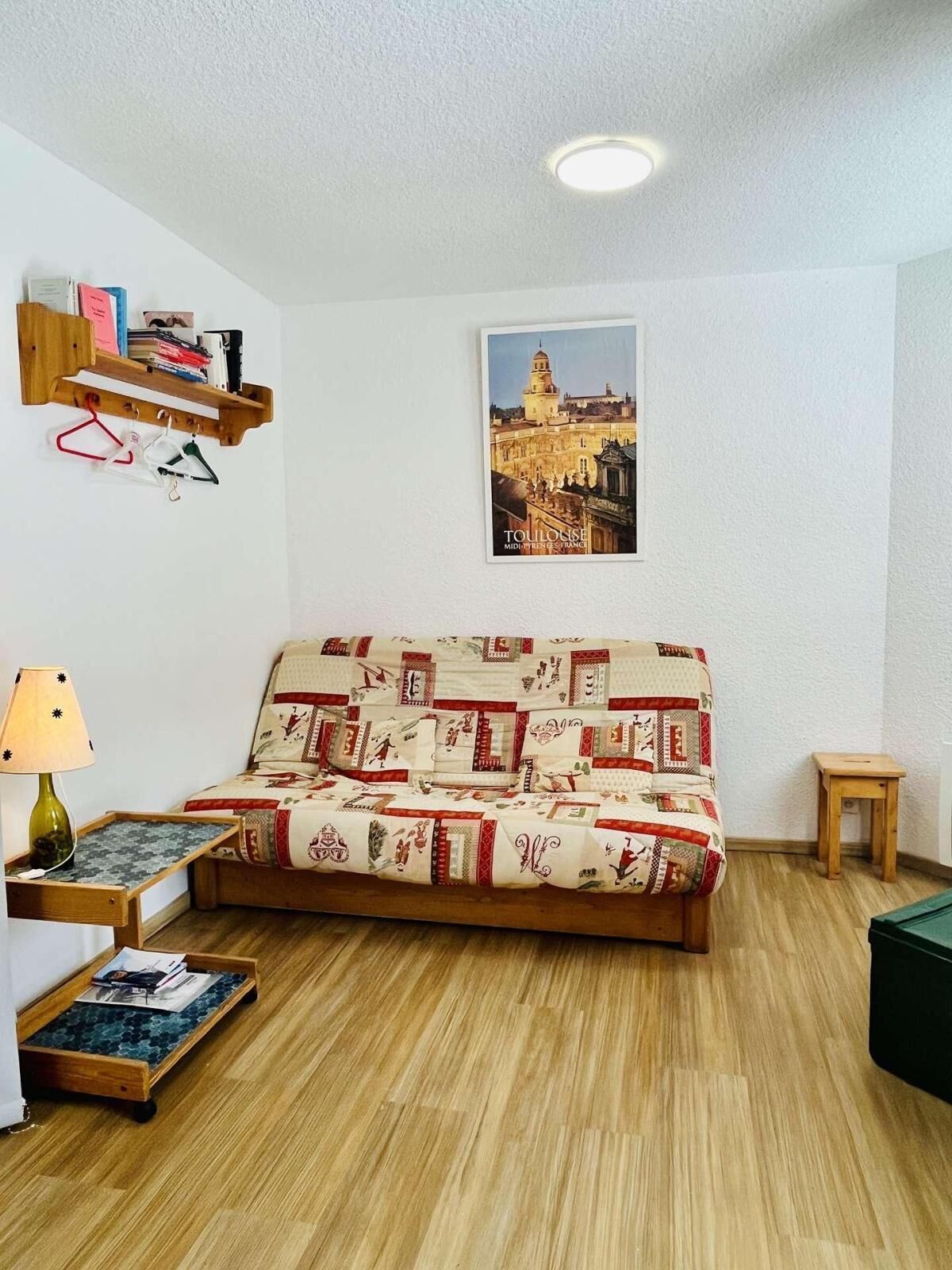 Un salon chaleureux avec un canapé à motifs, une petite table d’appoint en bois, une lampe et un tableau encadré représentant un paysage urbain accroché au mur.