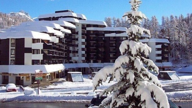 Un hotel de varios pisos con un diseño arquitectónico moderno, que cuenta con balcones y un paisaje cubierto de nieve.