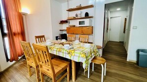 Comedor con una mesa lista para cuatro, sillas de madera, un microondas y estanterías sobre la mesa.
