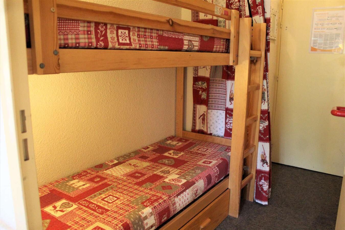 A bunk bed with a quilted bedspread, a wooden ladder, and a door with a notice on the wall.