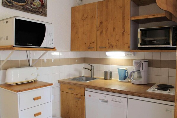 Une cuisine compacte dotée de meubles en bois, d’un four à micro-ondes, d’un grille-pain, d’un évier et d’un lave-vaisselle.