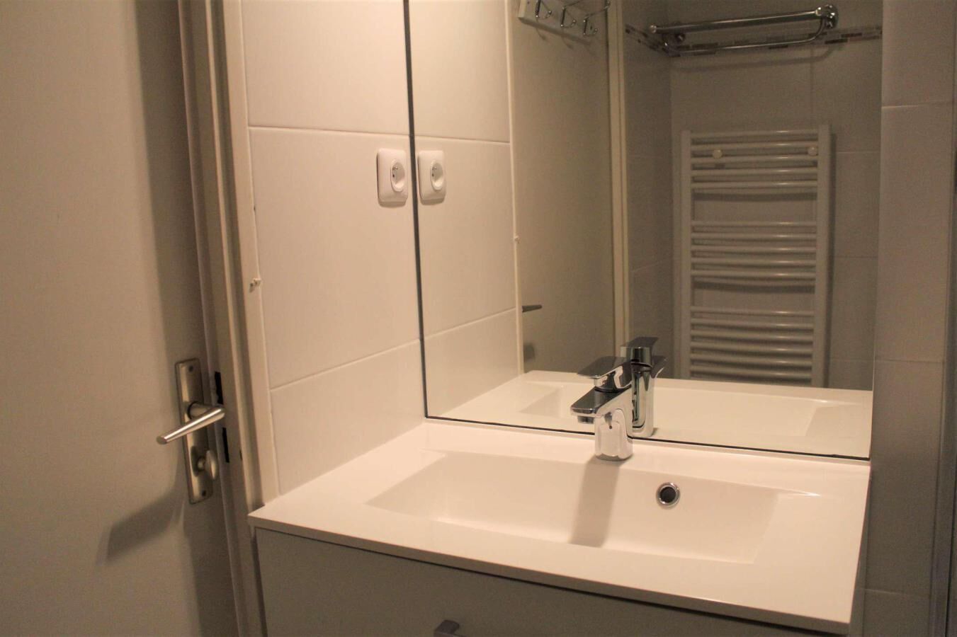 A bathroom with a white sink, a mirror, and a towel rack.