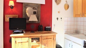 A room with a red wall, a wooden cabinet with a television, a lamp, and a small shelf with decorative items. - 350m from ski slopes, 3rd floor, balcony, 22m², Vars (Vars)