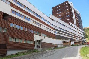 A multi-story building with a modern architectural design, featuring a combination of wooden and white exterior panels, and a visible entrance with a glass door.