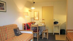 Un salon confortable avec un canapé à rayures, une petite table à manger avec des chaises, un four à micro-ondes et une poubelle.