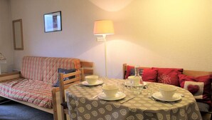 Une pièce chaleureuse avec une table à manger dressée pour quatre personnes, un canapé, une lampe et un tableau encadré au mur.