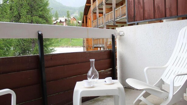 Un balcon avec des chaises blanches, une petite table et un vase.