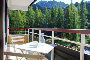 A balcony with a table and chairs, a white vase, and a mountain view.