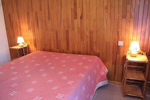 Una camera da letto con parete rivestita in legno, una coperta rossa con motivi bianchi e due lampade da comodino.