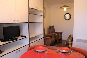 Un ambiente compatto con un tavolo da pranzo per due persone, una televisione e una piccola area salotto con una poltrona e un divano.