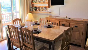 A dining area with a wooden table set for four, chairs, a lamp, and a wall-mounted TV. - Resort center, 3rd floor, balcony, tv, 30m², Vars (Vars)