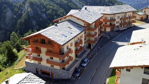Ein mehrstöckiges Hotel mit Balkonen, einer Steinfassade und Blick auf eine gebirgige Landschaft.