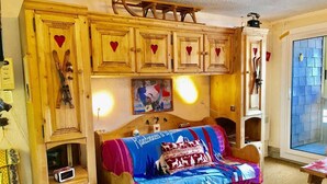 A cozy room with a wooden bed, built-in shelves with skis, a small TV, and a window with a view.