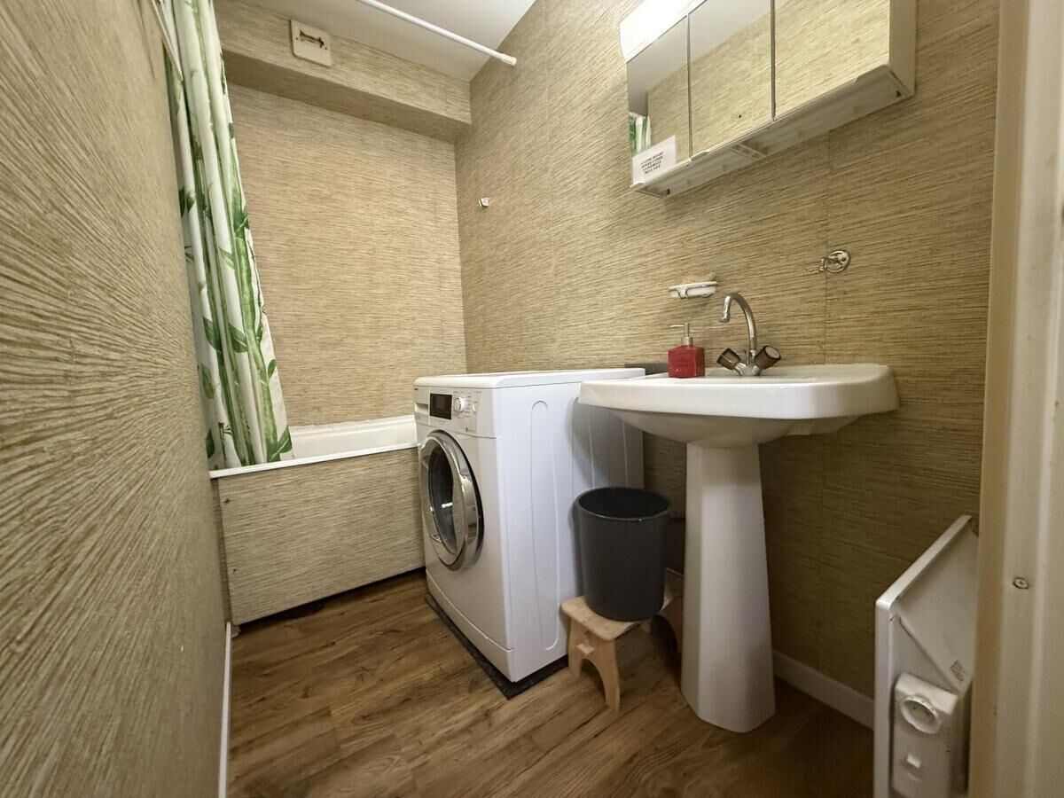 A compact laundry room with a washing machine, a sink, and a small stool.