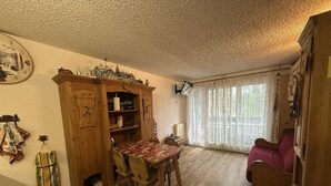 A cozy room with a wooden dining table, chairs, a wooden cabinet, and a window with sheer curtains.