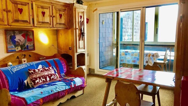 A cozy room with a wooden sofa, a dining table, and a large window.