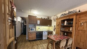A compact kitchen with wooden cabinets, a dining table with chairs, and a refrigerator.