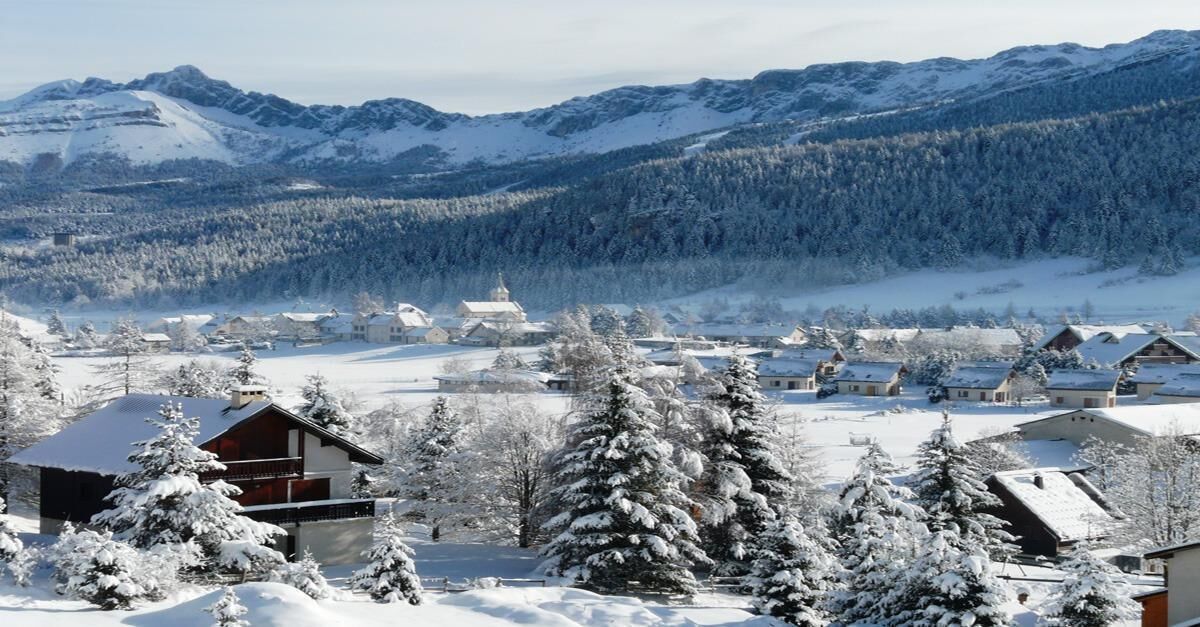 A snow-covered village with traditional wooden houses and a prominent church.