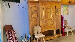 A room with a wooden cabinet, a small wooden chair, a television mounted on the wall, and a Coca-Cola vending machine.