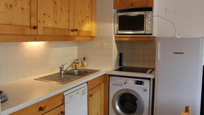 A compact kitchen with wooden cabinets, a built-in microwave, a dishwasher, and a sink.
