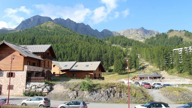 A mountain lodge with wooden cabins, a stone building, and a parking area with cars.