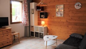 A cozy living room with a television, wooden furniture, a small table with a lamp, and a couch.