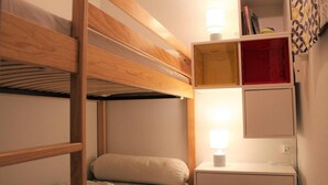 A bunk bed room with a nightstand, a shelf with books, and a lamp.