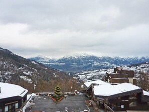 A hotel with a view of snow-covered mountains, a Christmas tree, and a parking area.