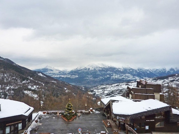 A hotel with a view of snow-covered mountains, a Christmas tree, and a parking area.