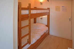 A bunk bed with a wooden frame, white bedding, a wall-mounted light, and a door with a notice on it.